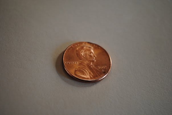 A single copper penny resting on a neutral gray surface, representing value